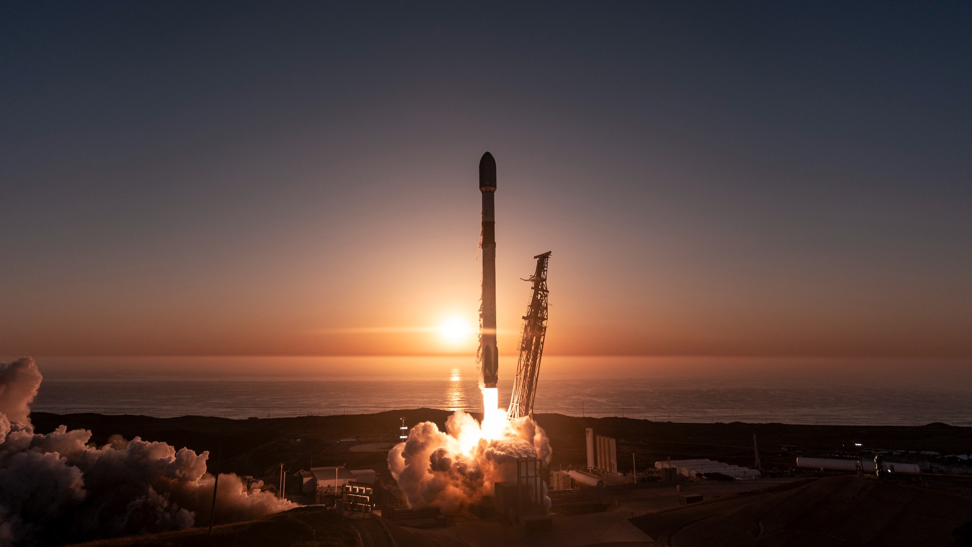 a rocket launches with the sunset over the sea behind it