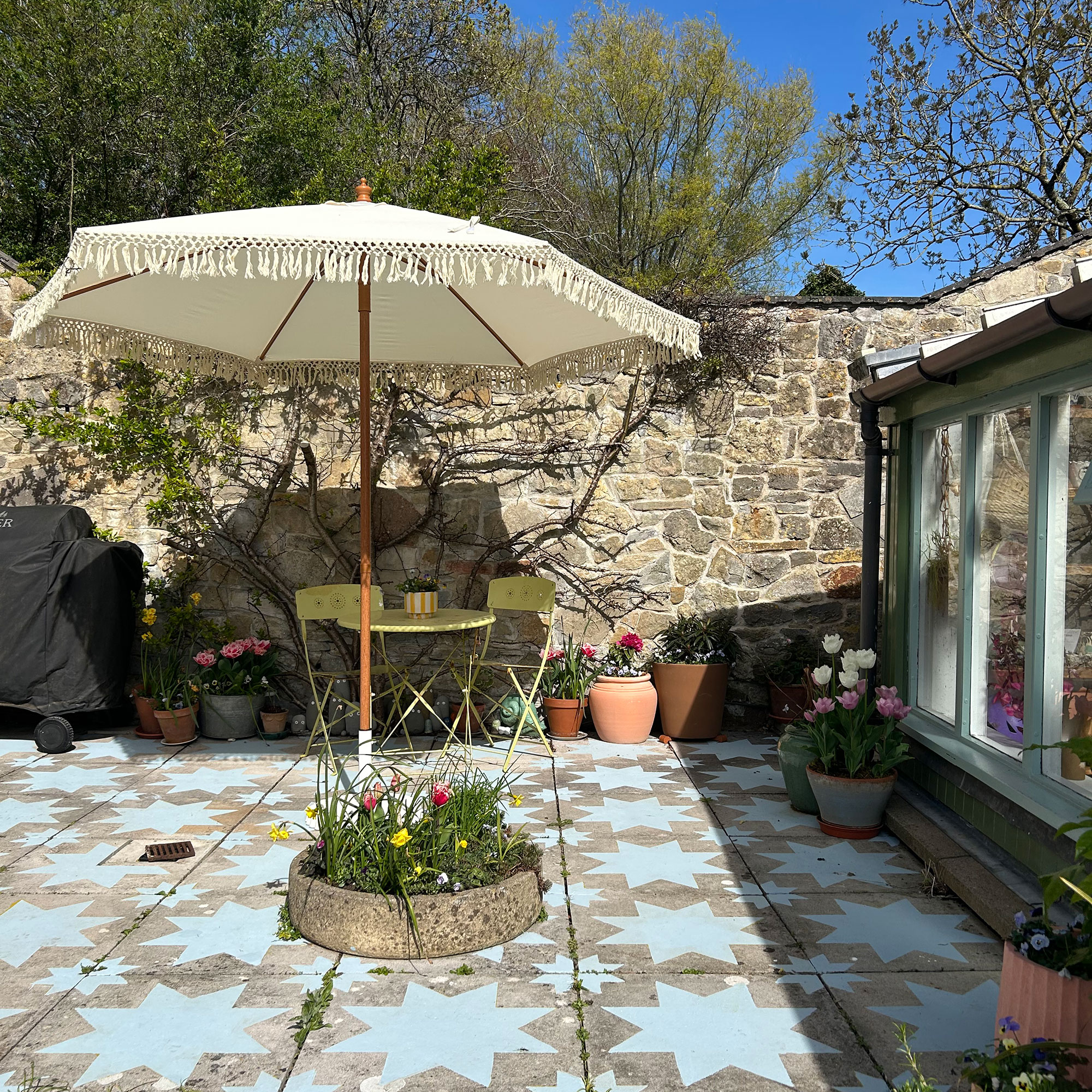 Stone wall enclosed patio with yellow bistro set, raised circular flower bed and slabs painted with blue star design