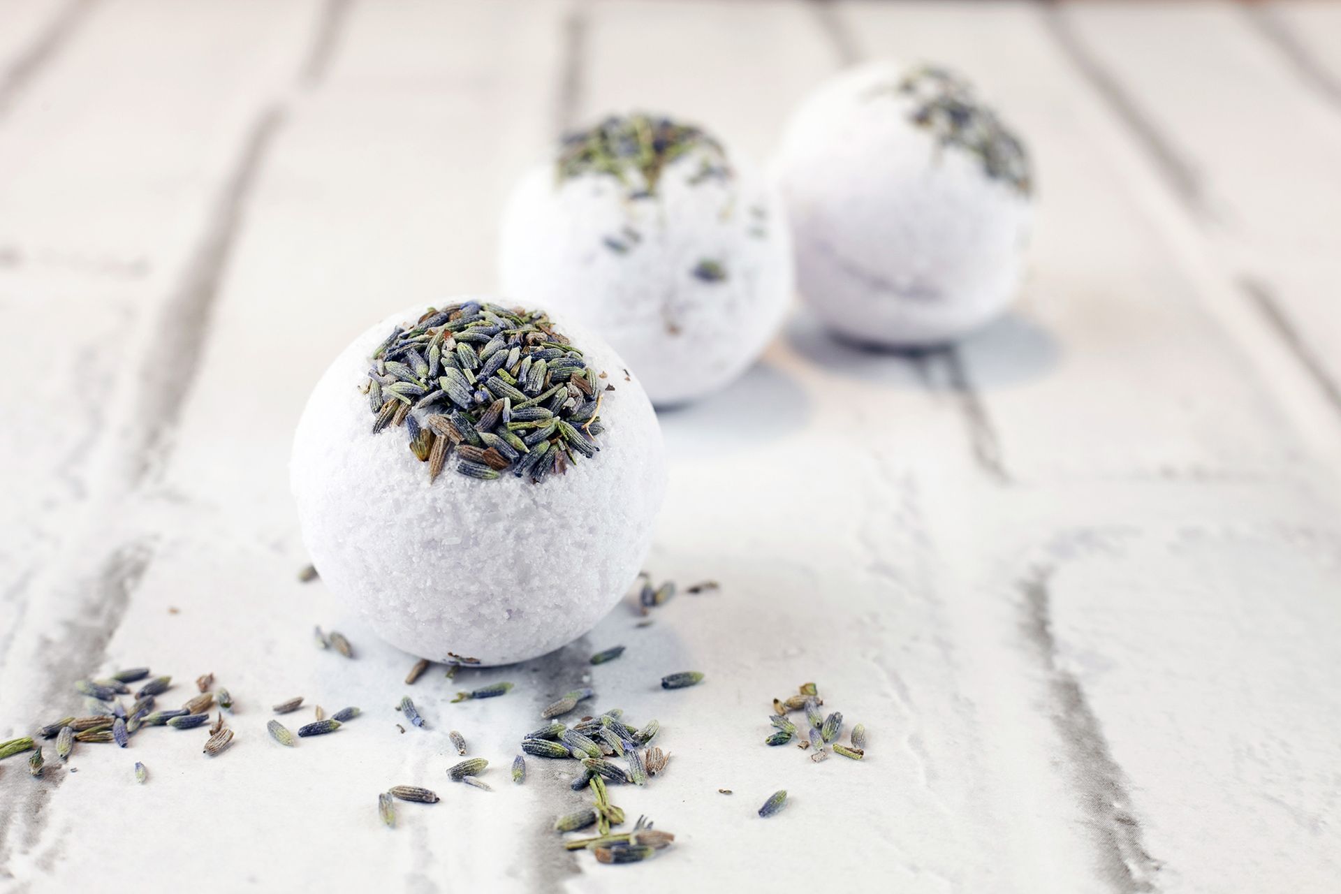 Three lavender bath bombs on a white brick background.
