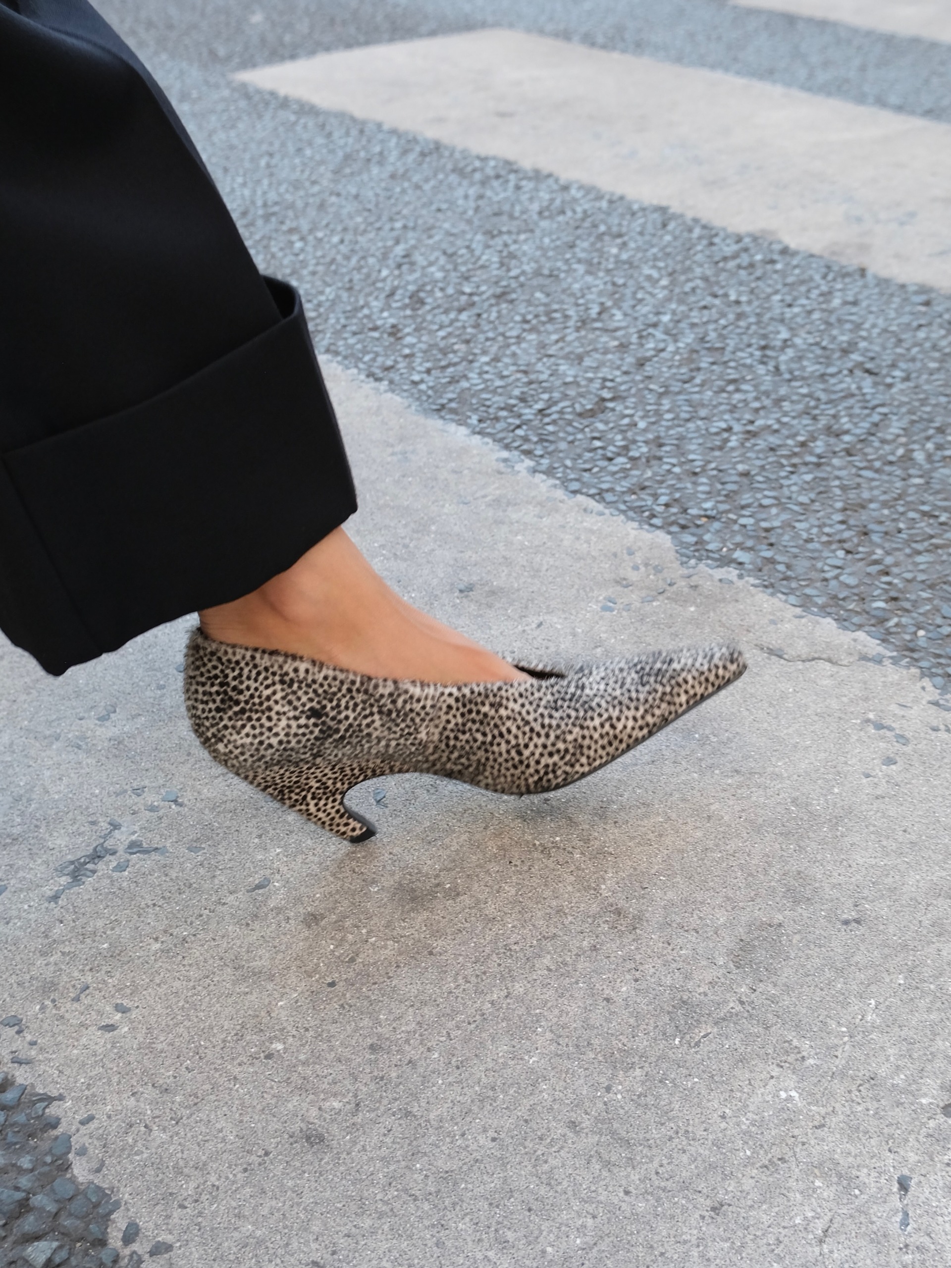 A closeup image of a French influencer's foot walking across a crosswalk wearing Dalmatian print high-vamp heels