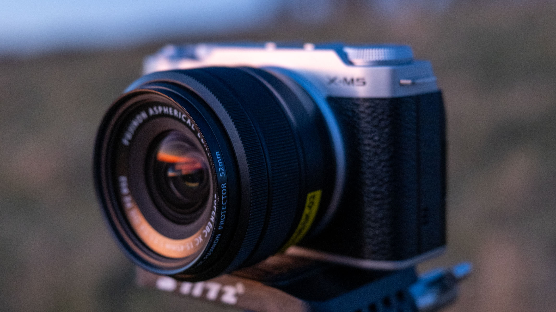 The Fujifilm X-M5 with an XC 15-45mm f/3.5-5.6 OIS PZ lens on a tripod head in a field