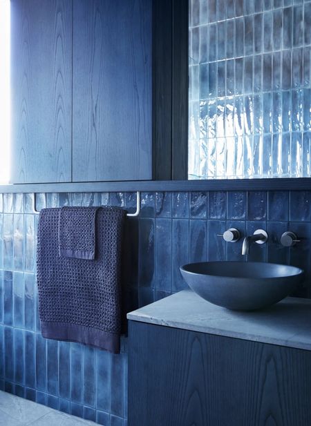 Image of a denim blue drenched bathroom with blue tiles, blue towels, a blue sink, and blue stained wooden cabinetry.