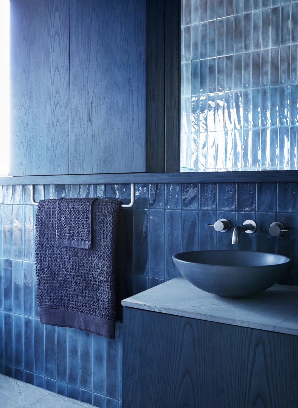 Image of a denim blue drenched bathroom with blue tiles, blue towels, a blue sink, and blue stained wooden cabinetry.
