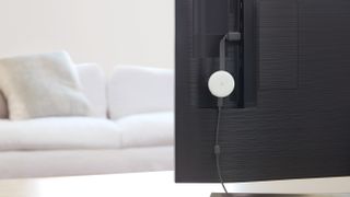 The Google Chromecast (3rd Generation) in white, hooked up to the back of a TV in a white living room.