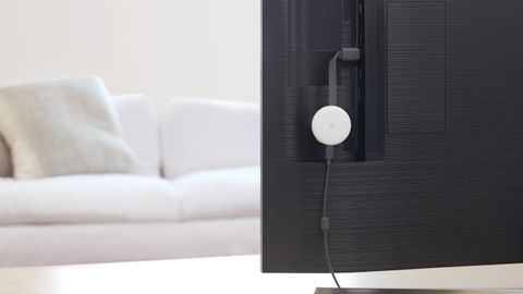 The Google Chromecast (3rd Generation) in white, hooked up to the back of a TV in a white living room.