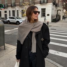 @jen_wonders on the streets of New York wearing a chic winter look with a black coat and a sweater worn as a scarf, styled with classic, elevated winter staples.