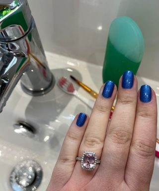 Morganite engagement ring on hand over white ceramic sink with toothbrush and fine art brush with green dish soap in background