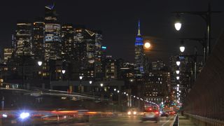 The full Worm Moon rises behind the skyline of midtown Manhattan and the Empire State Building in New York City as traffic drives down the 14th Street viaduct on March 25, 2024, in Hoboken, New Jersey.