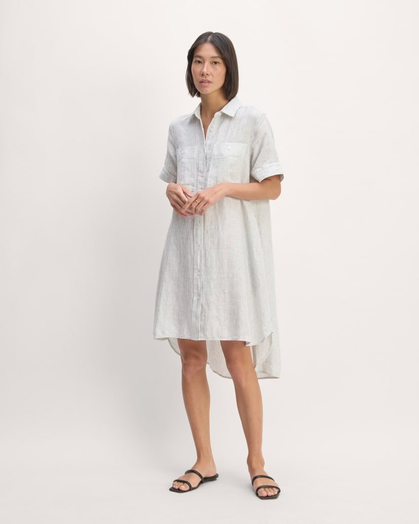 a model wears a loose-fitting shirtdress that hits at the knees and is longer in the back