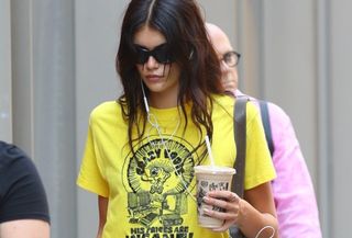 Kaia Gerber wearing a yellow graphic T-shirt with a white midi skirt and ballet flats in NYC.