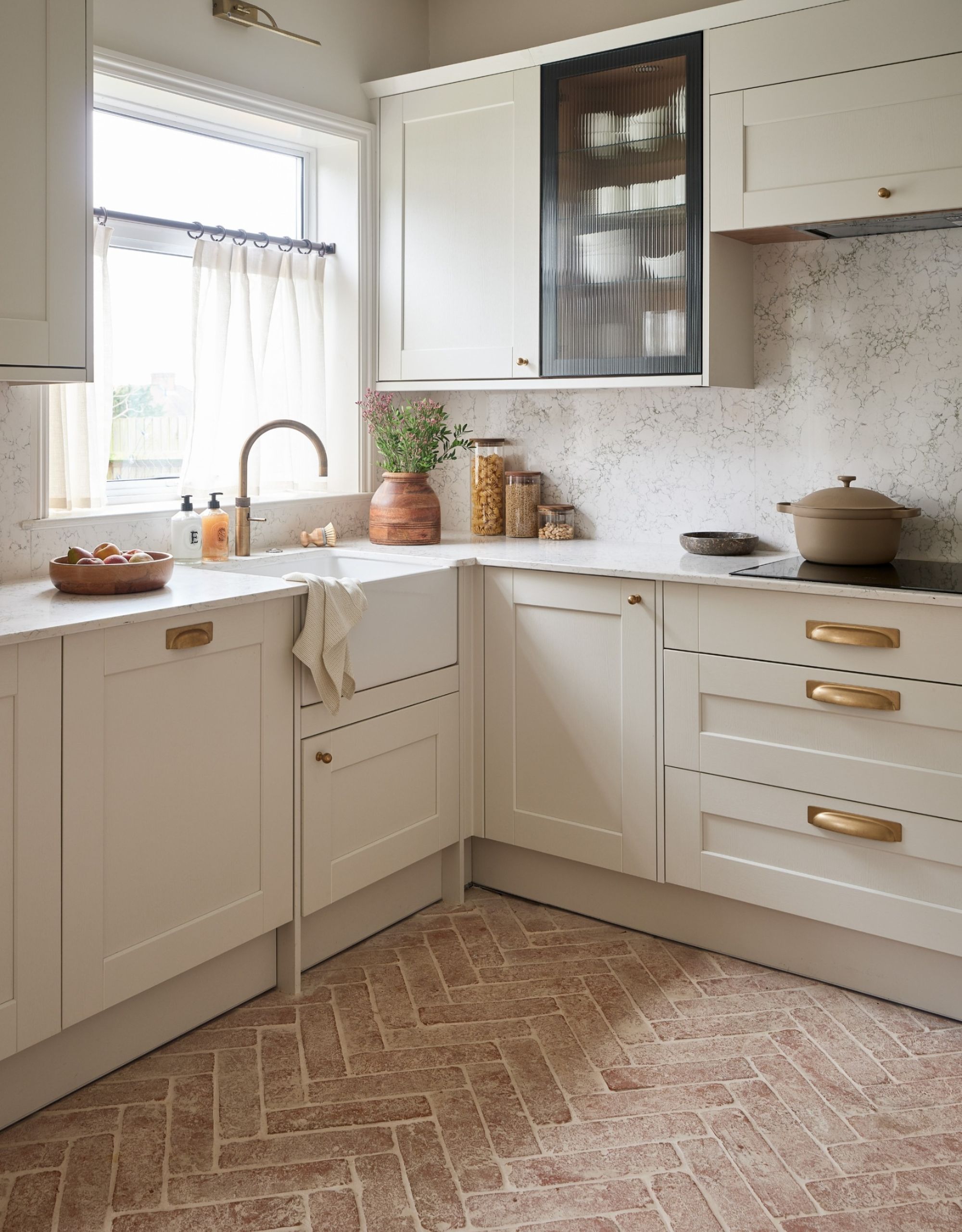 A warm neutral kitchen with brushed brass hardware and parquet terracotta floor tiles