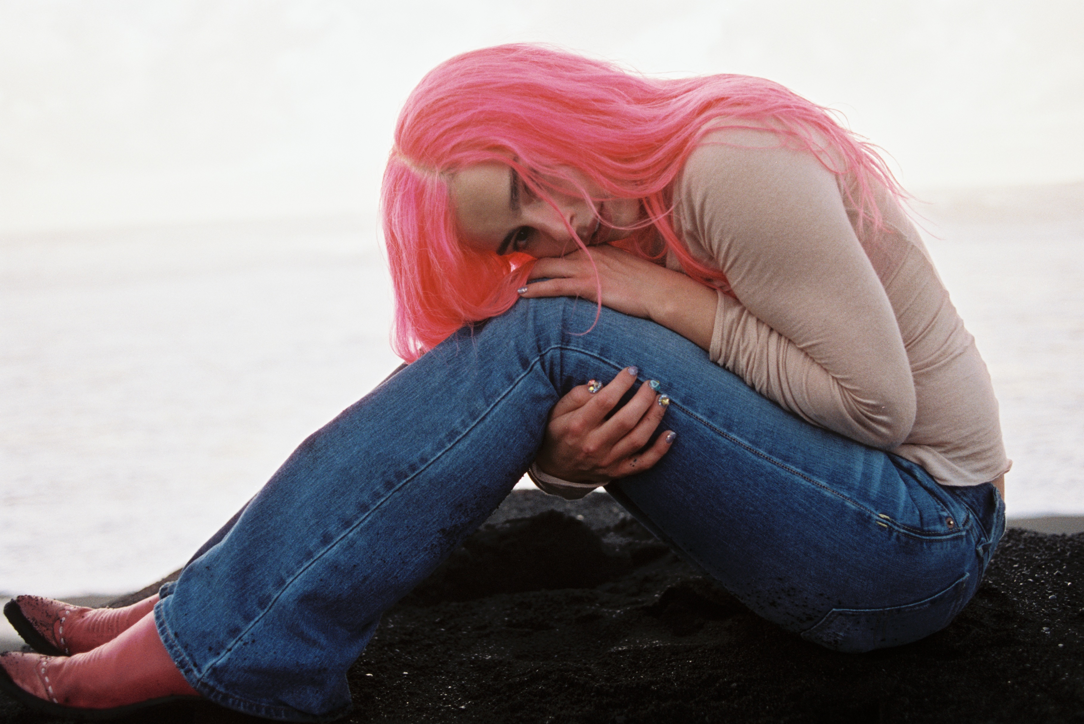 addison rae with pink hair sitting by the ocean in jeans