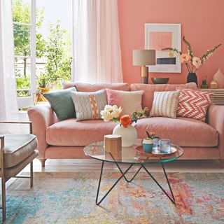 A peach-painted living room with a matching sofa and a round glass coffee table in front