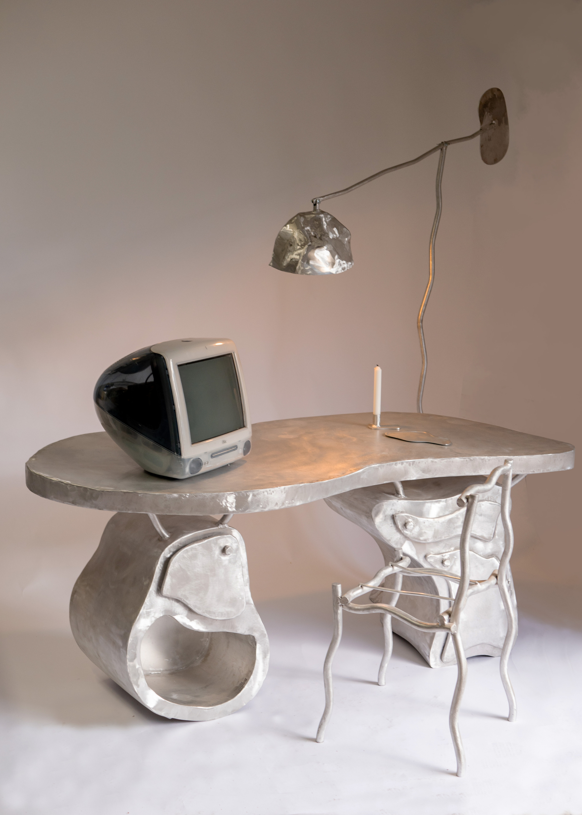 A brushed metal desk and chair with an old mac and a statement lamp