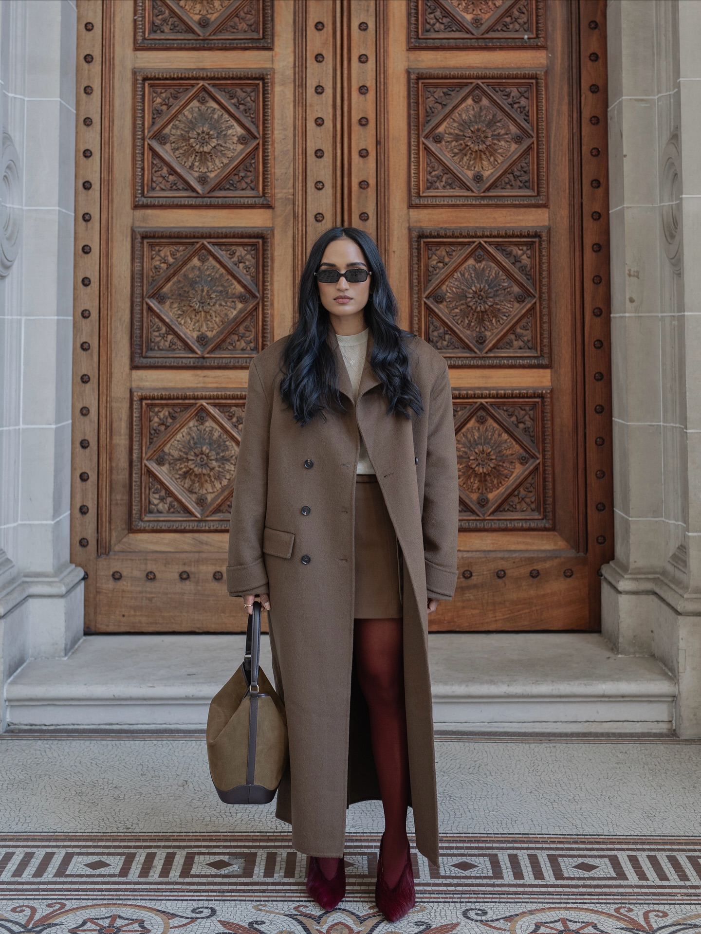 An image of @divrav wearing burgundy tights with a taupe ankle-length coat.