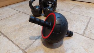 An ab roller next to a selection of kettlebells on a hard floor