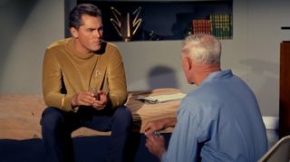 a man in a gold starfleet uniform talks to a doctor