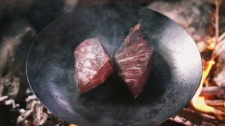 Two slabs of meat cooking in a frying pan