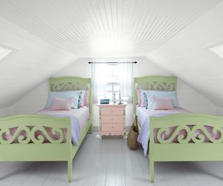 A white attic bedroom with light green single beds and a light pink side table between them.