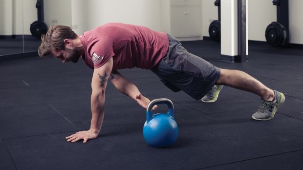 Man demonstrates plank drag with kettlebells