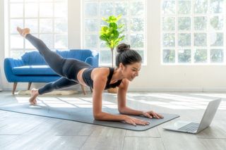 Fit woman doing Pilates and watching online tutorials on laptop, training in living room