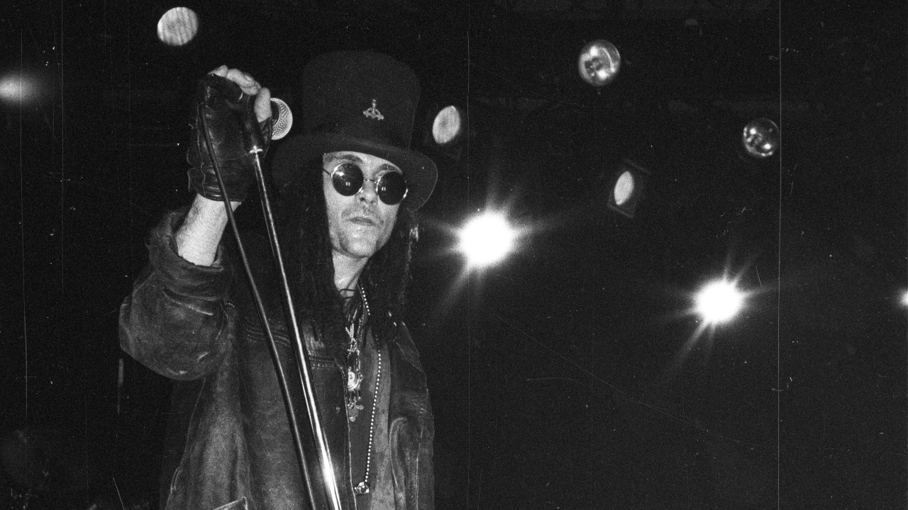 A black and white photo of Al Jourgensen on stage in 1996, in a top hat and shades
