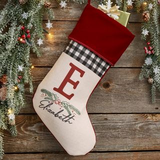 A white and red Festive Foliage Personalized Christmas Stocking hanging on a wooden mantel under a faux green garland