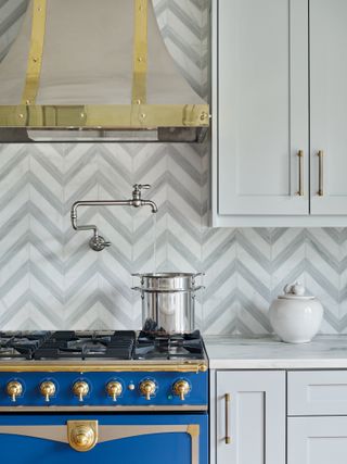 Kitchen cabinets in gray next to blue range and hood with geometric backsplash