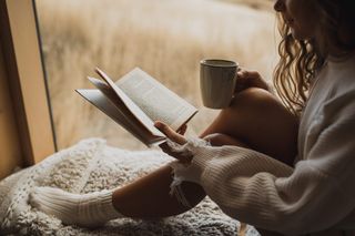 A woman reading a book and enjoying a warm drink for a blog article on autumn activities.