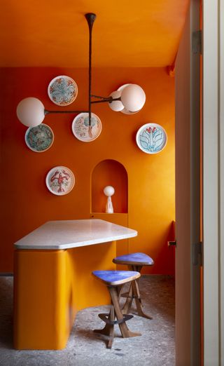 Interior of Pierre Yovanovitch Paris showroom, with orange walls, blue topped stools and plates on wall