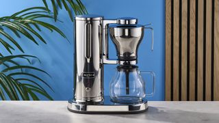 a silver drip brew coffee maker with a 10 cup capacity is photographed against a blue background