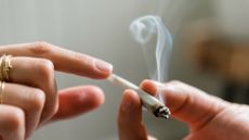 Close-up image of a joint being passed from one person's hands (on the right side of the image) to another (on the left side of the image). The hand on the left has a gold ringer on two fingers.