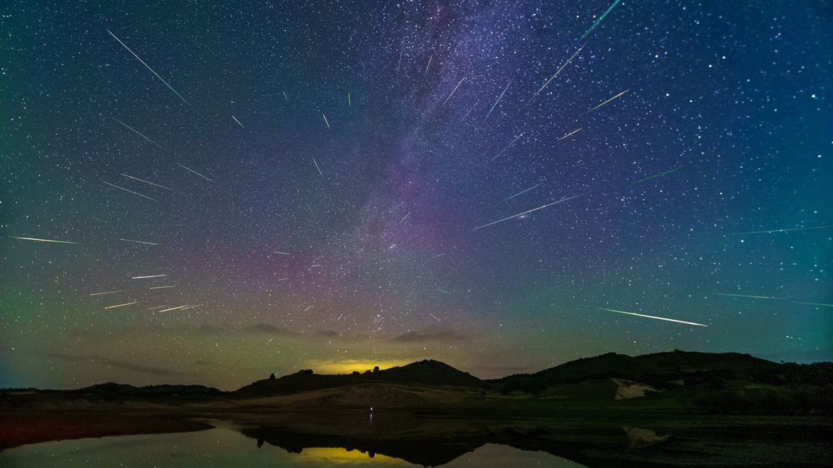 Perseid meteor shower appears as numerous long white streaks through the starry sky with some hills silhouetted in the distance. 