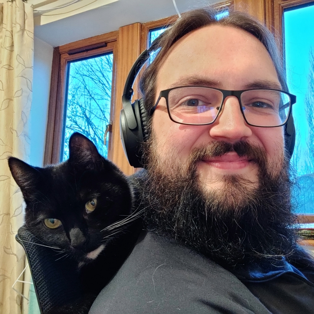 Toby Jackson smiling and wearing headphones with his cat Banjo behind him