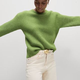 Image of woman wearing green jumper and white jeans 