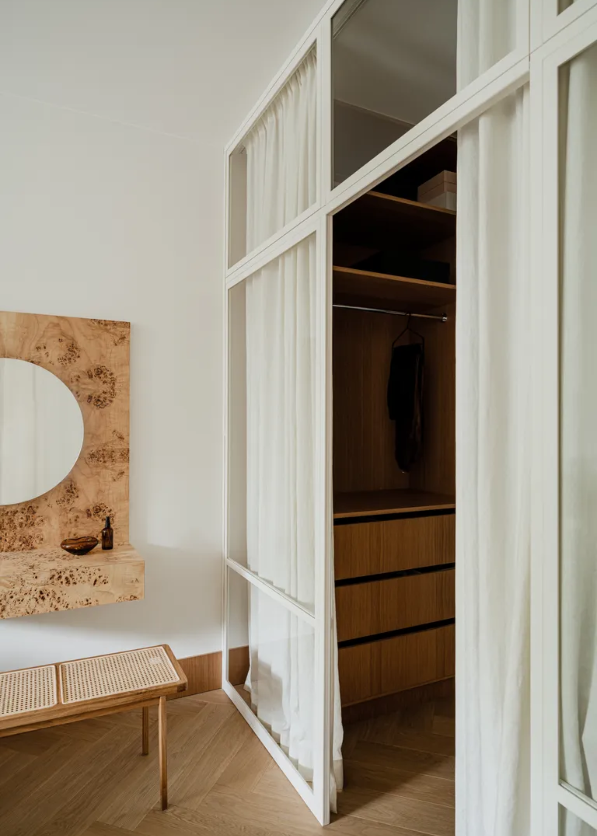 A walk-in wardrobe with a white curtain and a rattan bench near a wood mirror