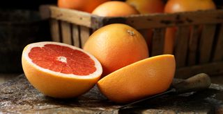 sliced grapefruit on a wooden surface in a garden in front of a basket of grapefruits to suggest how to attract birds that eat slugs for natural pest control