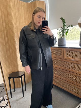 Woman in mirror wears black leather jacket, black tailored trousers