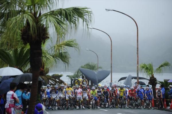 The peloton awaits the start of stage three in Taiji in front of a whale statue.