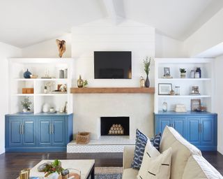 Subtly tiled fireplace hearth in white lounge with blue cabinets and white shelving