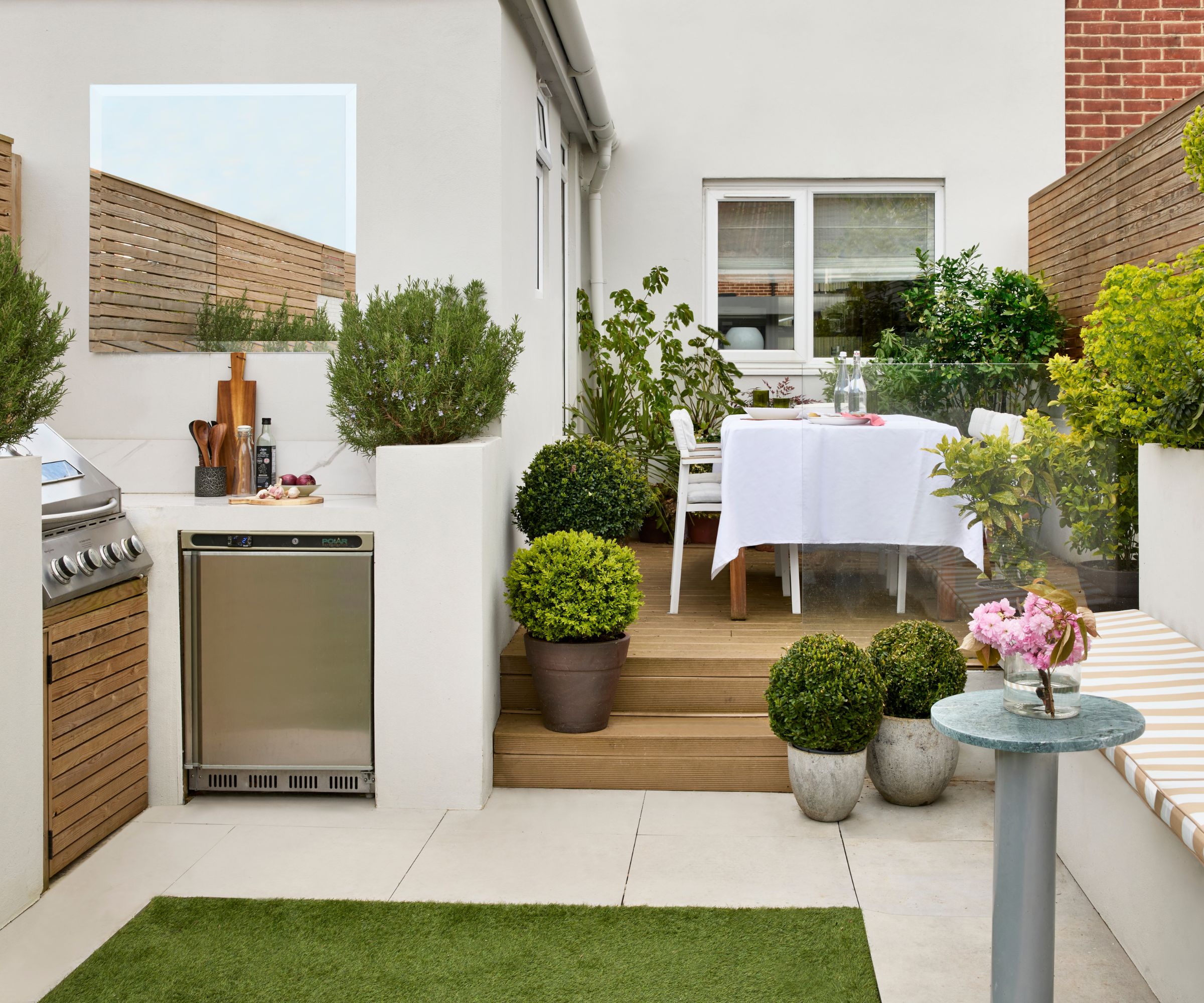 Outdoor kitchen and dining space in a small garden with striped banquette seating