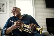 An older man laughs while hodling his trumpet.