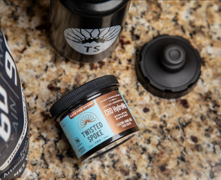 A turquoise and bronze 2500mg cylinder of CBD powder lays on its side atop a mottled tan and black stone countertop.
