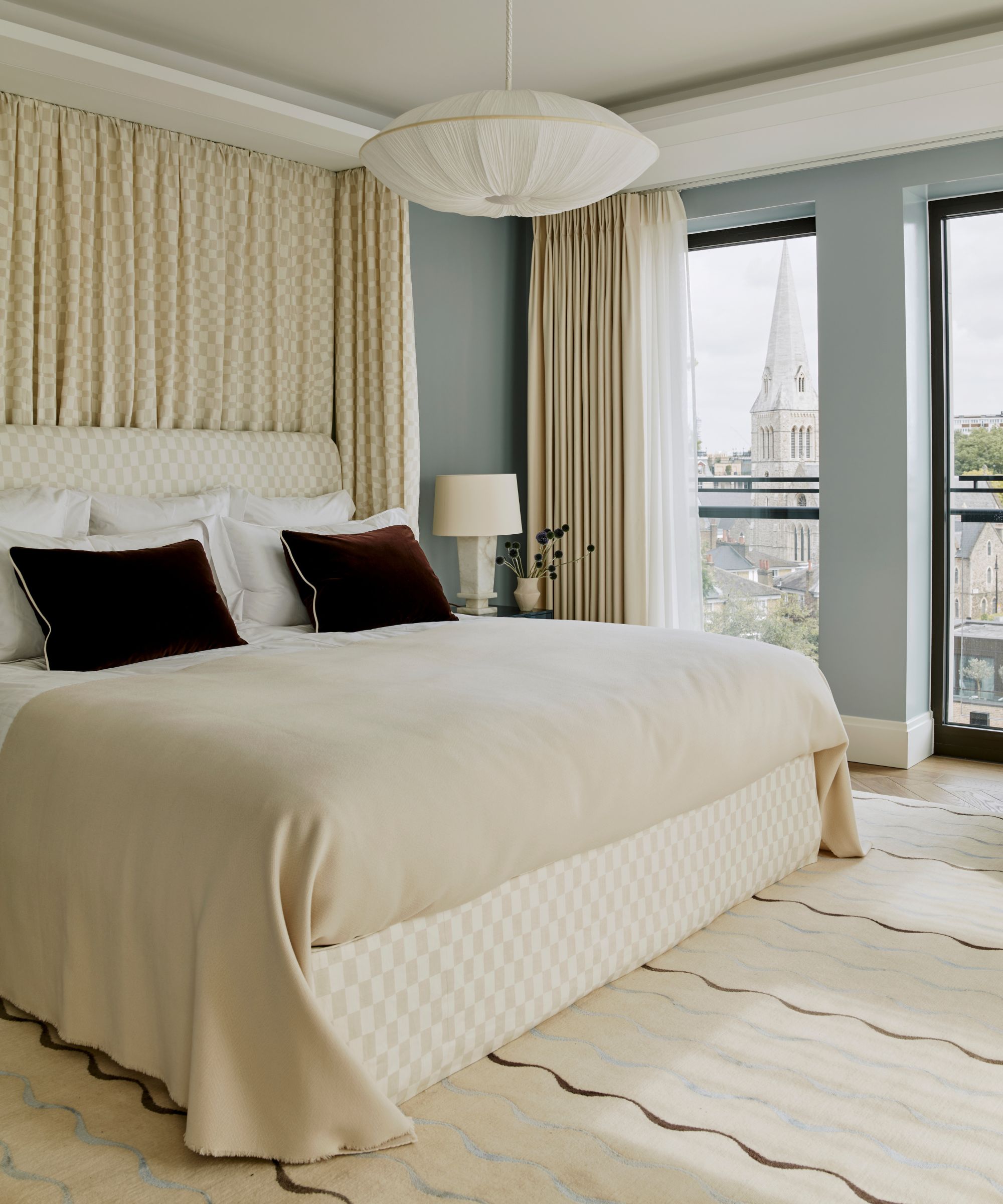 cozy modern light blue bedroom with large glass windows, a canopy bed, wiggle print rug and burgundy throw pillows on a neutral bed linen and throw