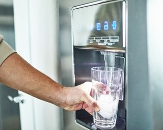 Man filling glass with ice and water from fridge dispenser