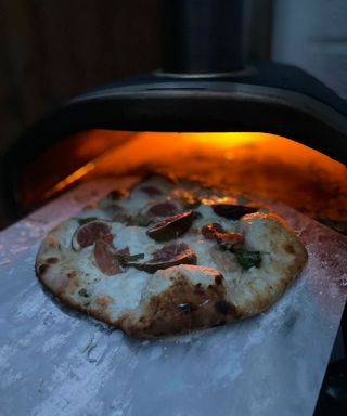 sliding a pizza into an outdoor pizza oven