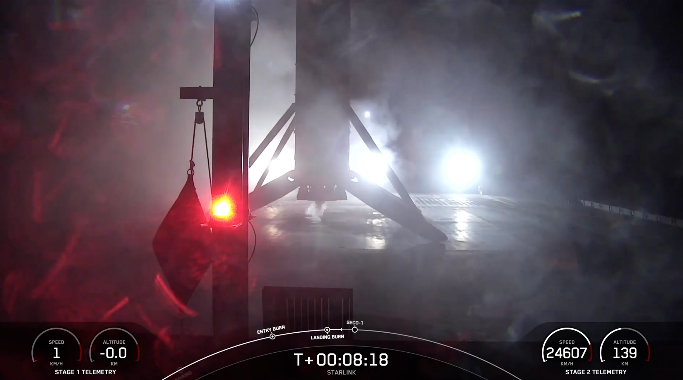 A black and white spacex falcon 9 rocket first stage sits on the deck of a ship at sea at night