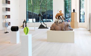 A wider look at the gallery room. We see a sculpture of a boy in the back, two sculptures on the stand of a green shell and a hollow black cylinder. Further back we see a sculpture of animals stacked one on another.