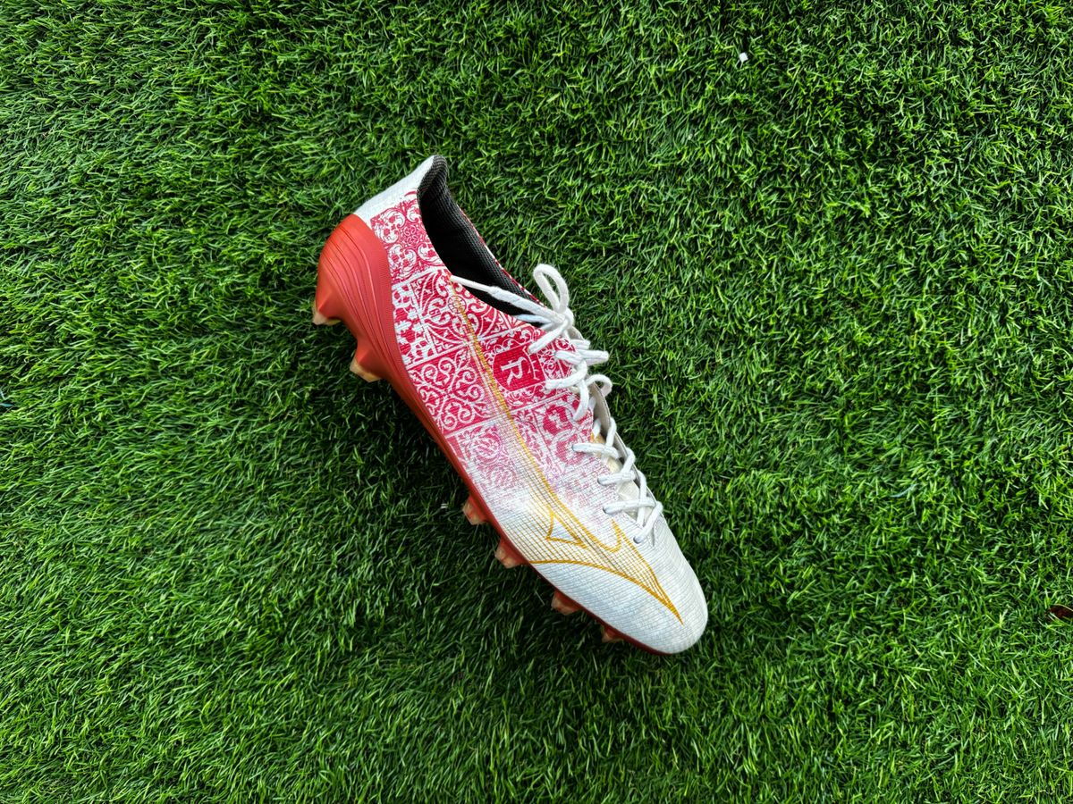 Mizuno Alpha Made in Japan football boots placed on some astro turf Red and white football boots side by side with one the right way up and the other on its side, both on green artificial grass.