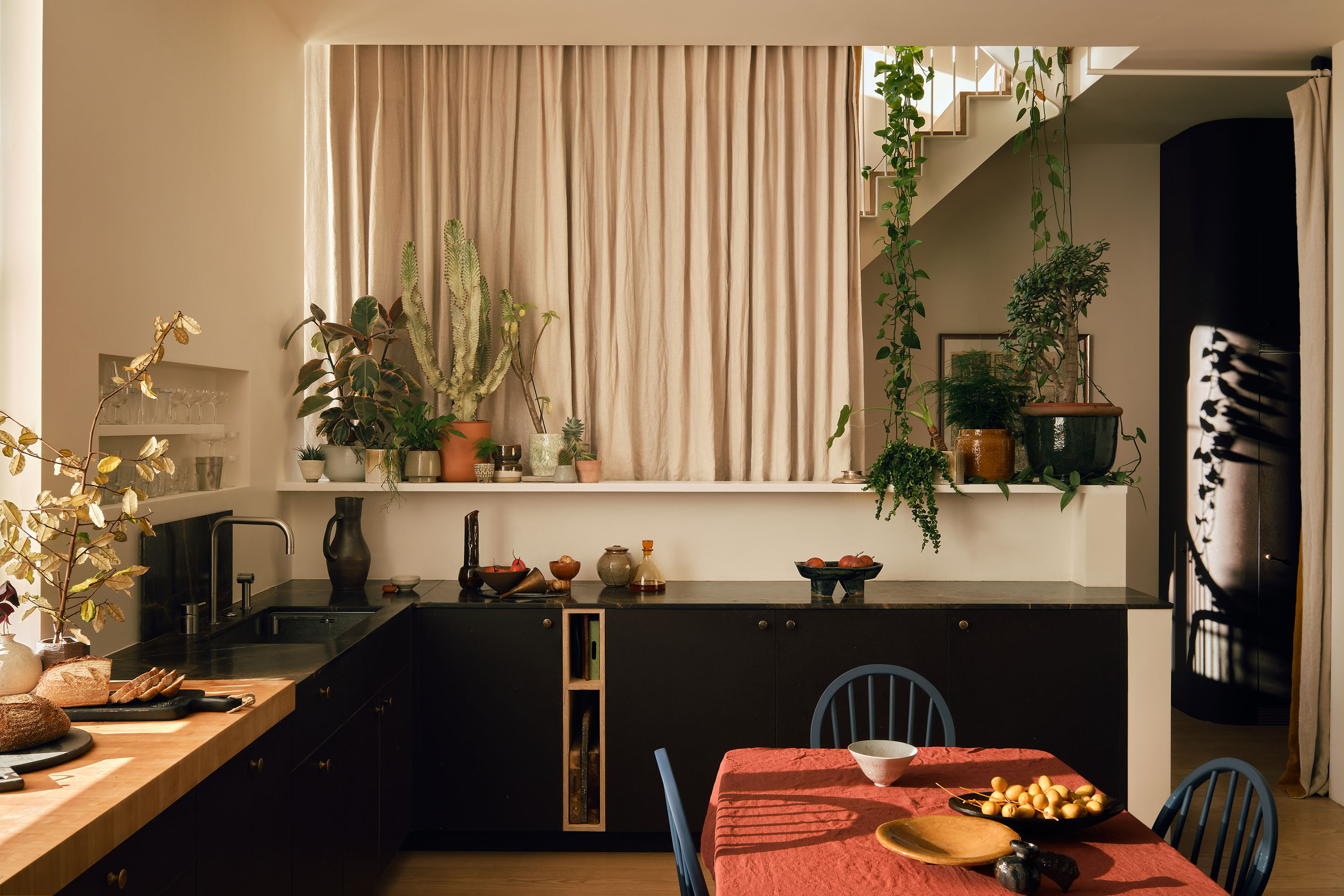 Interiors of a beautifully designed, spacious home with wooden floors, neutral decor, and lots of colorful accessories and furniture, including thriving plants and a golden-glowing paper lamp.